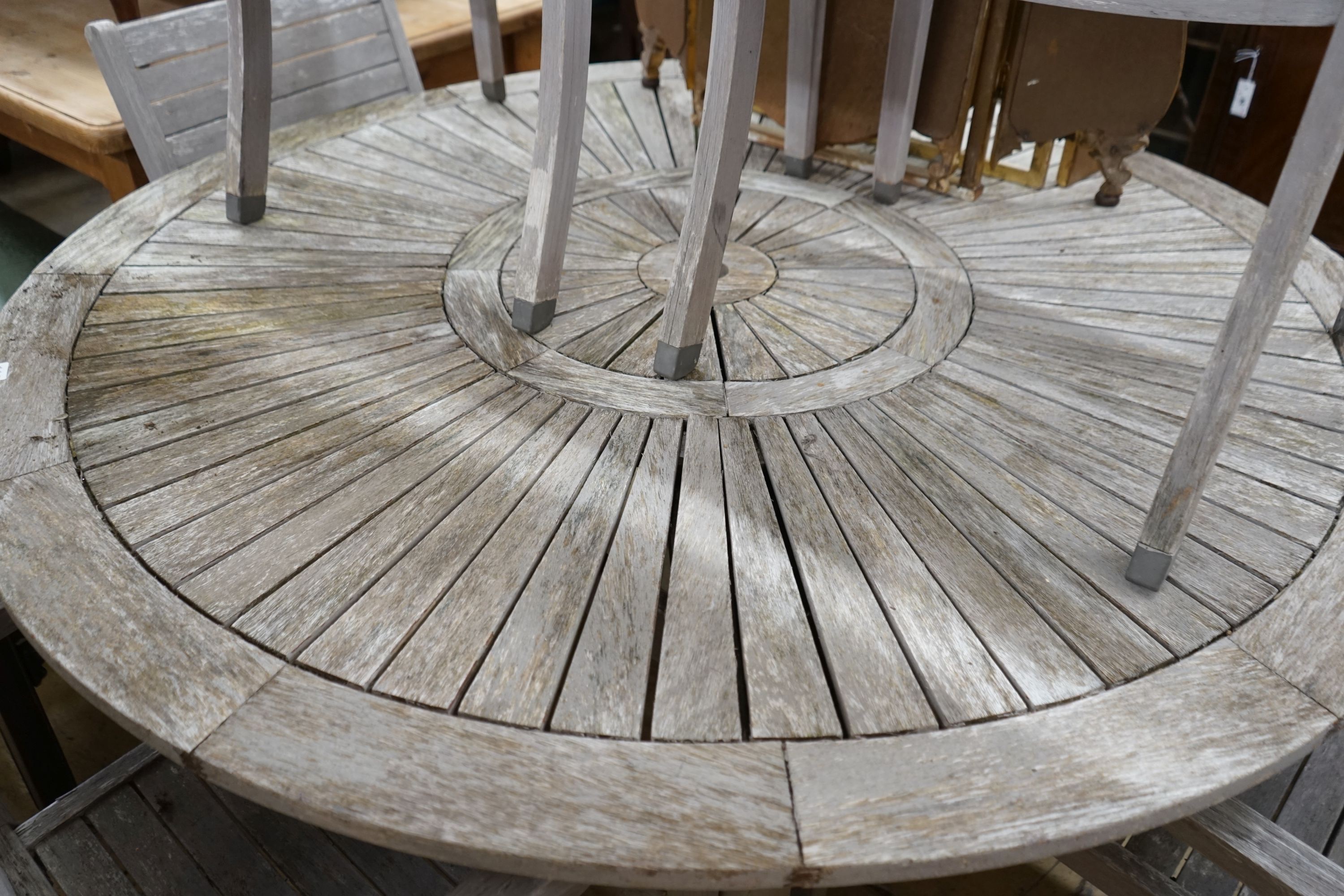 A circular weathered teak garden table, diameter 153cm, height 75cm together with six weathered teak stacking garden elbow chairs